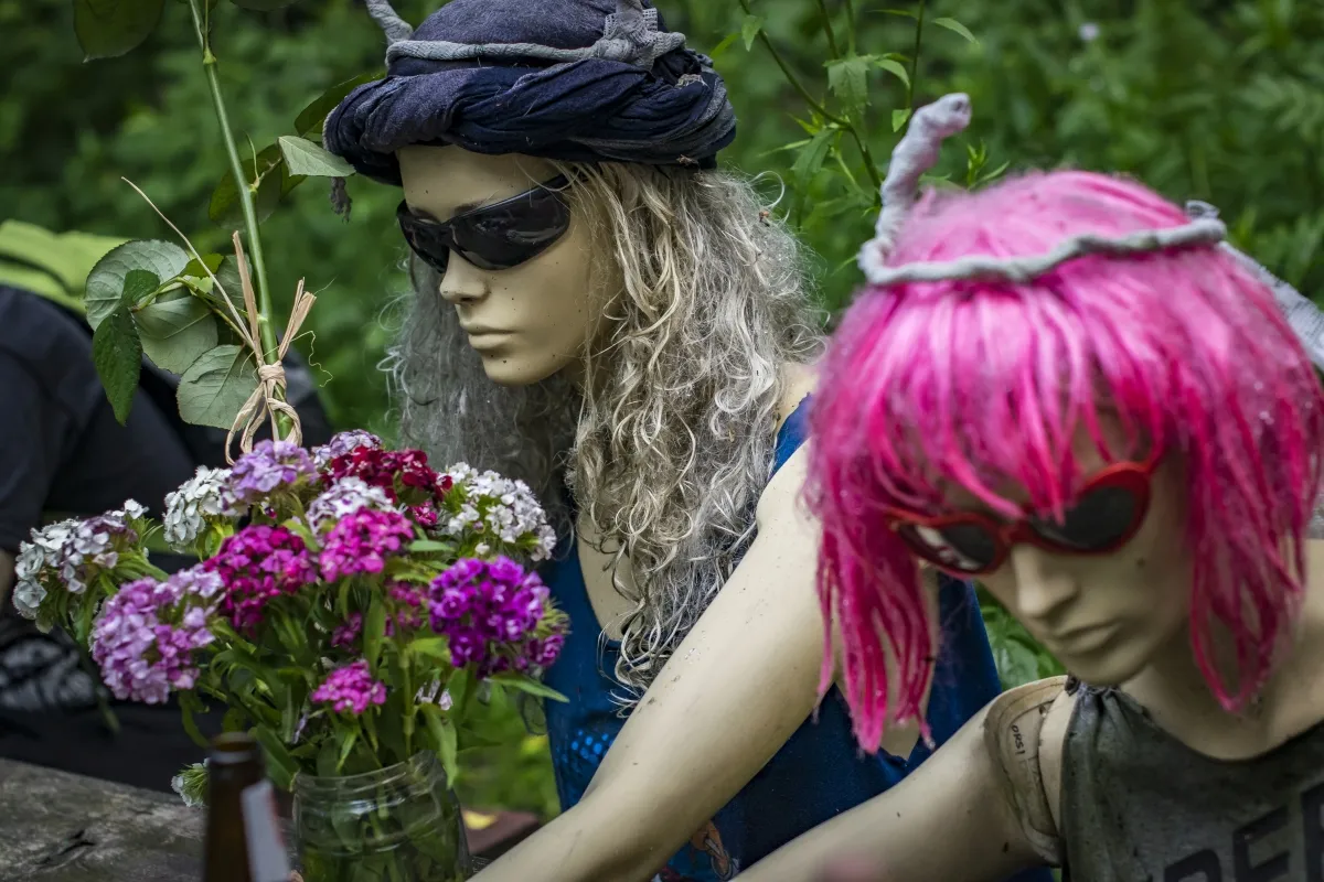 Two mannequins in wigs and sunglasses posed beside flowers